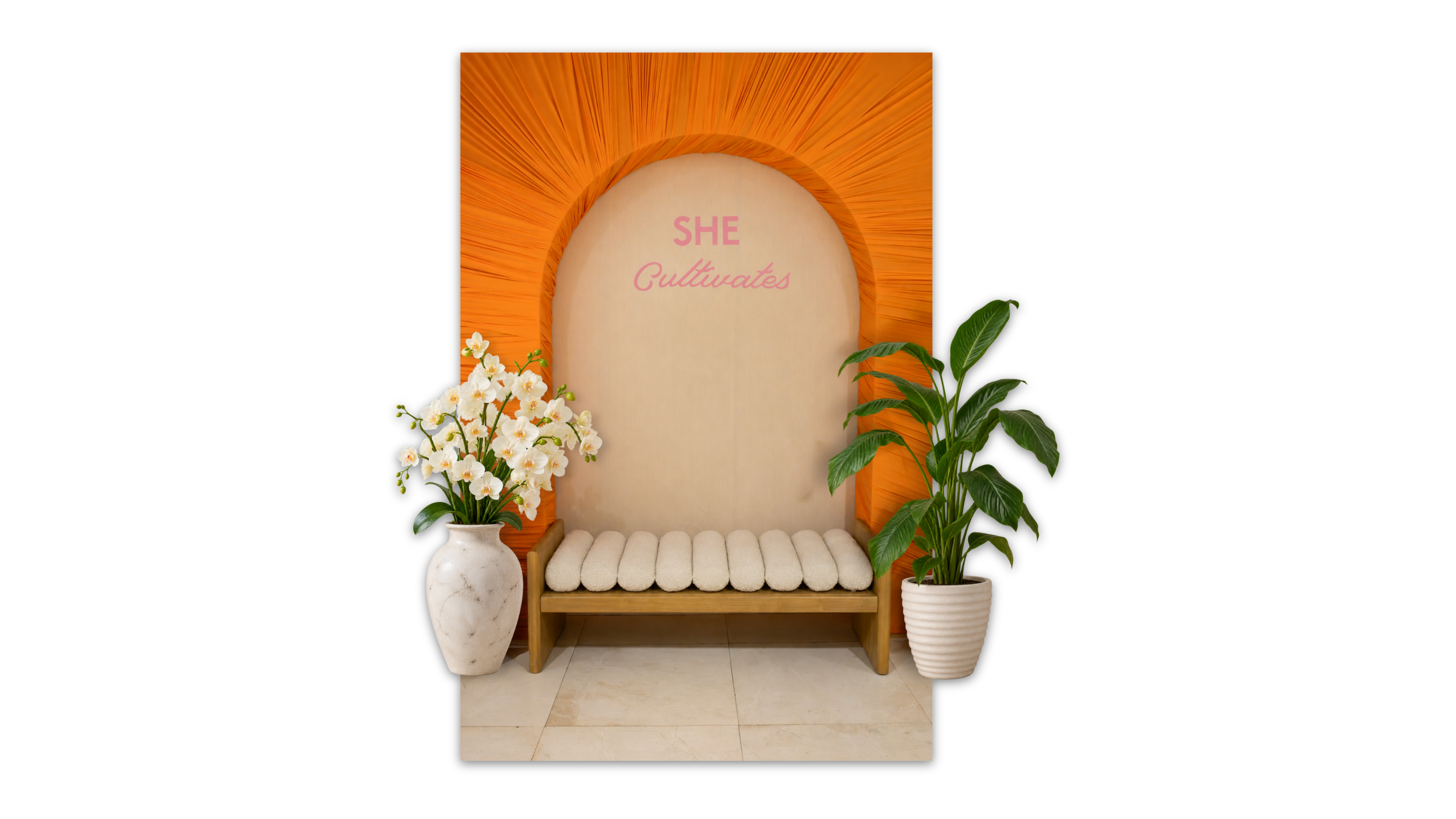 She Cultivates photo backdrop with orange sunburst draping, pink lettering, and a white bouclé bench